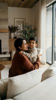 Happy South Asian mother hugging her laughing toddler son in a cozy modern living room, sharing a warm, joyful family moment at home.