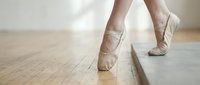 Close-up of ballet dancer's feet en pointe on wooden studio floor, wearing soft pink pointe shoes. Professional dance training and performance.
