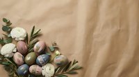 Colorful painted Easter eggs nestled with eucalyptus branches and white flowers on soft beige fabric background for spring holiday celebrations.