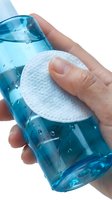 Hand holding blue glass bottle with water droplets while applying white cotton pad for cleaning and skincare routine.