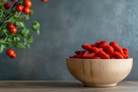 Dried goji berries in wooden bowl with fresh berries on branch, superfood antioxidant nutrition concept on dark background for healthy lifestyle content.