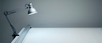 Adjustable desk lamp with metal arm positioned above empty white workspace, suitable for office and study environments.