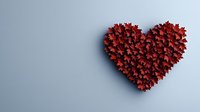 Red maple leaves arranged in heart shape on light gray background, casting soft shadow. Creative romantic nature concept for valentines and love themes.