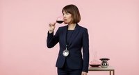Professional female sommelier in navy business suit tasting red wine against pink background for wine industry and tasting events.