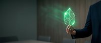 Businessman in dark suit holding glowing green leaf symbol, representing sustainable business practices, environmental responsibility, and eco-friendly corporate innovation in modern office setting.