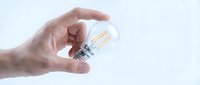Caucasian male hand holding a clear LED filament light bulb against a white background, symbolizing innovation and bright ideas.