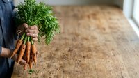 Farmer holding fresh organic carrots with green tops in hands, displaying harvest produce for farmers market, agriculture, and healthy food concepts.