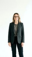 Professional woman with shoulder-length brown hair and glasses wearing charcoal blazer over olive shirt with black pants, isolated on white background for corporate and business design use.
