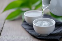 Pouring hot green tea from white teapot into ceramic cup on dark cloth with fresh leaves creating peaceful zen moment for relaxation and mindfulness.