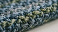 Close-up macro shot of textured knitted fabric with intricate stitch patterns in blue and green yarn colors showing detailed craftsmanship and textile artistry.