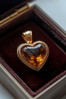 Golden heart-shaped pendant with amber gemstone in luxurious jewelry box. Elegant wire wrapped design showcases brilliant cognac crystal against velvet background.