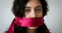 Young Middle Eastern woman with curly dark hair and red silk ribbon covering mouth symbolizing censorship, silence, and freedom of speech restrictions.