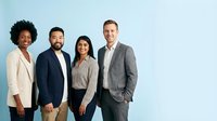 Diverse professional business team of four colleagues standing together in modern office attire against clean background for corporate presentations.