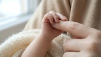 Newborn baby hand gently grasping adult finger in tender moment of connection and bonding between parent and child in soft natural light.