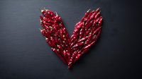 Dried red chili peppers arranged in heart shape on dark black background, dramatic lighting creates contrast and texture. Food styling for spicy cuisine concept.