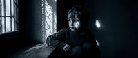 Young boy sitting alone in dark room with dramatic window light creating shadows on wall conveying loneliness depression and emotional distress in moody atmosphere.