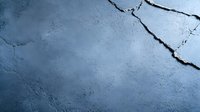 Cracked concrete wall surface with deep fissures and rough texture in moody blue lighting, creating dramatic shadows and depth for architectural backgrounds.