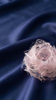 Tangled translucent fiber ball resting on deep blue fabric with soft folds, showcasing texture and material contrast for design and textile projects.