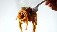 Delicious spaghetti pasta twirled on fork with rich tomato sauce and fresh herbs, ready to eat Italian cuisine meal on white background.