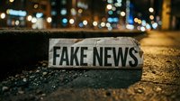 Fake news newspaper headline on urban street at night with bokeh city lights background representing misinformation and media literacy concepts.