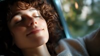 Young woman with curly hair relaxing with closed eyes and gentle smile, natural sunlight creating soft bokeh effect through window in peaceful moment.