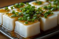 Cold tofu blocks topped with savory sauce and fresh green onions on wooden serving tray, traditional Asian appetizer ready to serve.