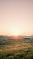 Sunrise over rolling hills with golden wheat fields and distant farmhouse, warm light casting long shadows across rural landscape for travel and nature projects.