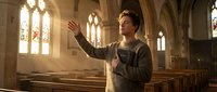 Young Caucasian man with raised hand speaking passionately in gothic church interior with wooden pews and stained glass windows during golden hour lighting.