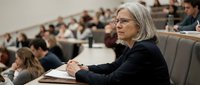 Mature Caucasian female professor teaching in university lecture hall with students attending academic seminar or educational conference presentation.