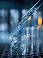 Glass pipette dropping liquid into laboratory beaker with bubbles forming in solution against blurred blue scientific background.