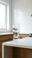 Three stacked geometric crystal glasses on white kitchen counter with subway tile backsplash and wooden cabinetry, modern interior design.