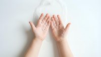 Young woman cupping hands with flour spilling down on white background for baking cooking kitchen preparation culinary arts food ingredient concept.
