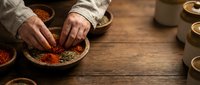 Hands arranging colorful spices in wooden bowls on rustic table. Traditional cooking preparation with paprika, herbs and seasonings for culinary recipes.
