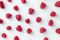 Fresh ripe raspberries scattered on white background in minimal pattern design. Perfect for healthy eating, food blogs, and summer berry promotions.