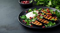 Grilled eggplant slices with yogurt sauce, fresh herbs and pomegranate seeds served on black plate against dark background. Mediterranean cuisine.