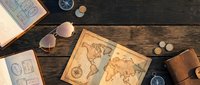 Vintage world maps and travel accessories arranged on dark wooden surface with compass, sunglasses, and passport for adventure planning and exploration themes.