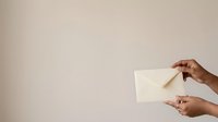 Hands holding blank cream envelope against neutral beige background, suitable for mail, correspondence, invitation, and business communication concepts.