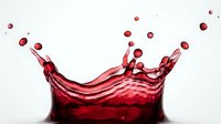 Red wine splash with dynamic droplets and crown formation against white background for beverage advertising and culinary design projects.