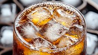 Refreshing cola drink with ice cubes in glass, condensation droplets on surface, fizzy bubbles and amber liquid close up macro photography for beverage advertising.