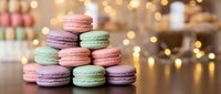 Colorful French macarons stacked in pyramid arrangement with warm bokeh lights creating festive bakery atmosphere for dessert and confectionery designs.
