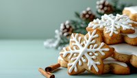 Festive snowflake sugar cookies decorated with white royal icing, displayed with pine cones, cinnamon sticks and evergreen branches on mint green background.