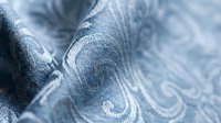 Closeup of blue fabric with ornamental swirl pattern and soft texture, suitable for textile design, fashion backgrounds, and interior decor projects.