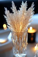 Delicate white crystal grass stems in elegant cut glass vase with warm candlelight creating romantic atmosphere for winter wedding or holiday celebration.