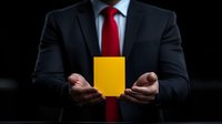 Businessman in dark suit and red tie holding yellow card against black background, dramatic lighting emphasizes professional warning concept.