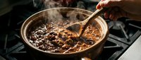 Homemade chili con carne simmering in copper pot with wooden spoon, steam rising from hearty bean stew on stovetop for comfort food recipes.