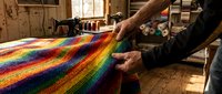 Artisan hands weaving vibrant rainbow striped textile on traditional loom in rustic workshop. Handcraft fiber art creation process for home decor and fashion.