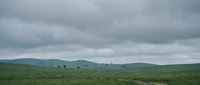 Rolling green hills under dramatic cloudy sky in rural countryside landscape with overcast weather conditions for nature and travel concepts.