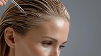 Young Caucasian woman with wet slicked back blonde hair and natural makeup having hair treatment procedure with metal clips against gray studio background.