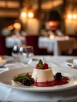 Elegant panna cotta dessert with fresh berries and mint leaves served on white plate in upscale restaurant setting with romantic ambient lighting and table settings.