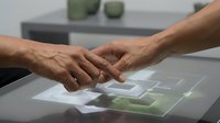 Two hands touching over interactive digital touchscreen display with glowing interface elements in modern technology environment for business presentations.